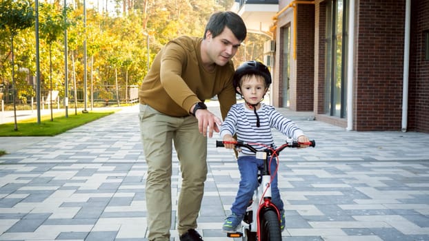 Handsome young amn teaching his little son riding his first bicycle at park.
