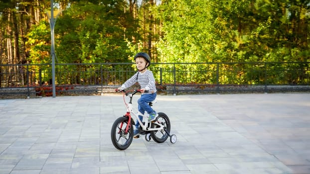 Little 3 years old boy in protective helmet riding his first bicycle at park.