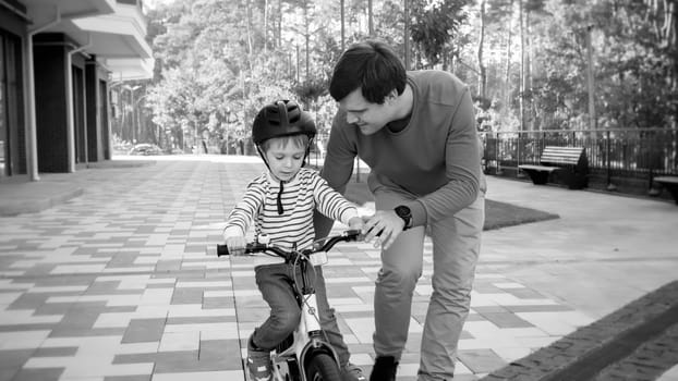 Black and white portrait of young man teaching his son driving his first bicycle.