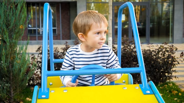 Happy smiling boy riding in big toy car on children playground.