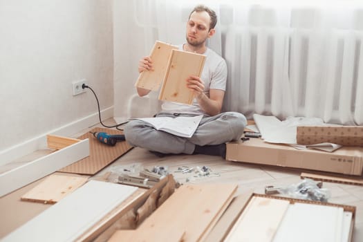 Man self-assemblies wooden furniture at home without master. Read instructions. Man reading instructions. Diy concept.