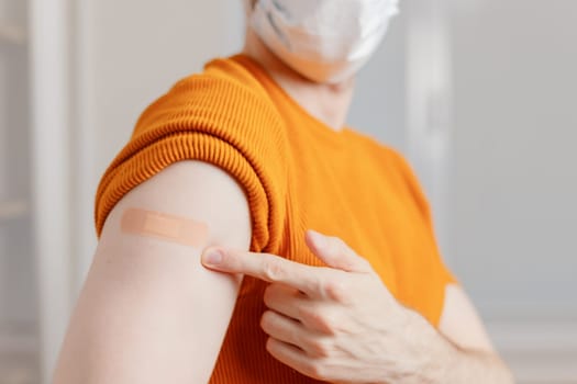 Man in mask showing his shoulder with bandage after getting a vaccination during covid-19 immunization program.