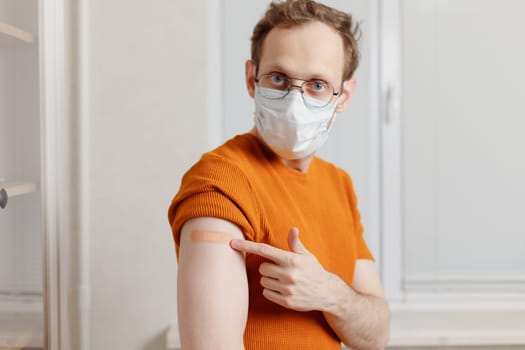 Caucasian young man showing his shoulder with bandage after getting a vaccination during covid-19 immunization program