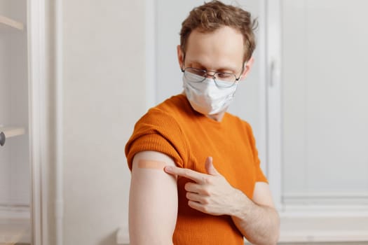 Caucasian young man showing his shoulder with bandage after getting a vaccination during covid-19 immunization program