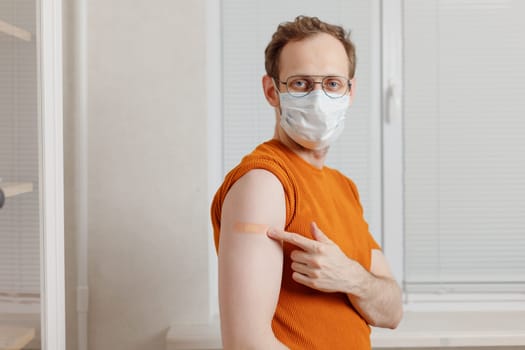 Senior caucasian man holding up shirt sleeve to show the sticking plaster after a covid-19 jab in shoulder