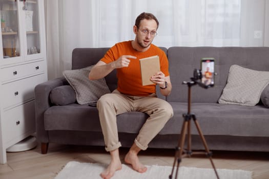 Handsome man blogger at home presents book while video stream. Social media marketing and online sales.