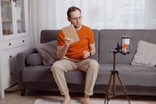 Handsome man blogger at home presents book while video stream. Social media marketing and online sales.