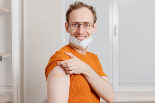 Caucasian young man showing his shoulder with bandage after getting a vaccination during covid-19 immunization program.