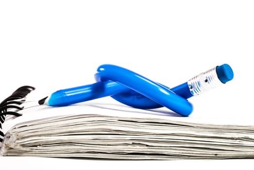 A blue pencil with a blue eraser on the end is bend, and tied in to a knot, and placed on top of a small white notebook.
