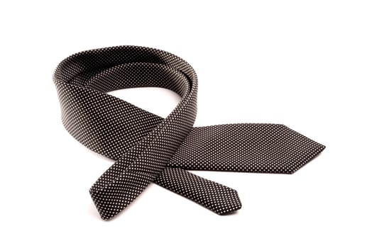 a neatly folded black tie with small white dots lies in a curve on a white isolated background.