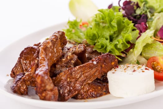 Fresh salad with fresh goat cheese and fried beef strips prepared on a plate insulated against a white background