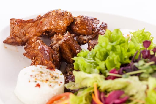 Fresh salad with fresh goat cheese and fried beef strips prepared on a plate insulated against a white background