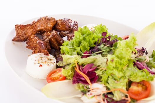 Fresh salad with fresh goat cheese and fried beef strips prepared on a plate insulated against a white background