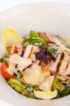 Fresh delicious caesarsalat with grilled chicken bust parmesan shards and croutons isolated against a white background