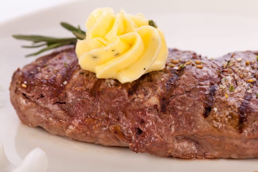 Succulent grilled beef fillet steak with homemade herb butter on a plate isolated against a white background