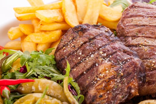 Huge barbecue plate with mixed meat and steaks on salad isolated against a white background