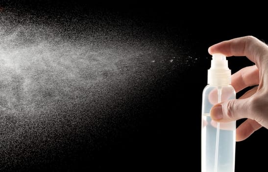 Man hand with a spray bottle of water on a black background.