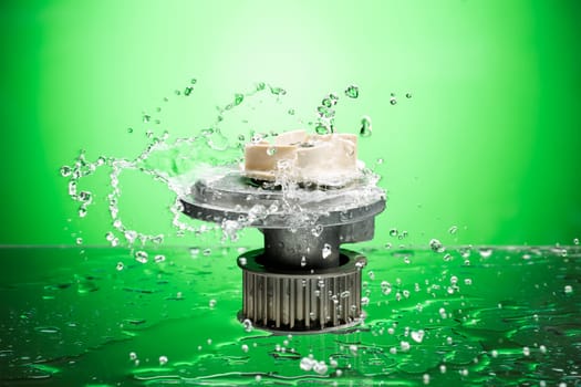 Auto parts, engine cooling pump in water splash on green gradient background