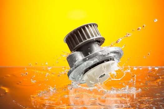 Auto parts, engine cooling pump in water splash on orange gradient background