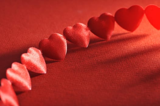 Chain of small red fabric hearts on a red background