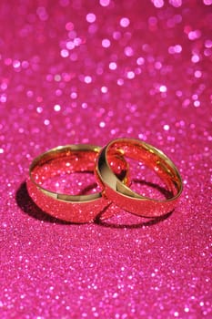 Two gold rings on a pink glitter background