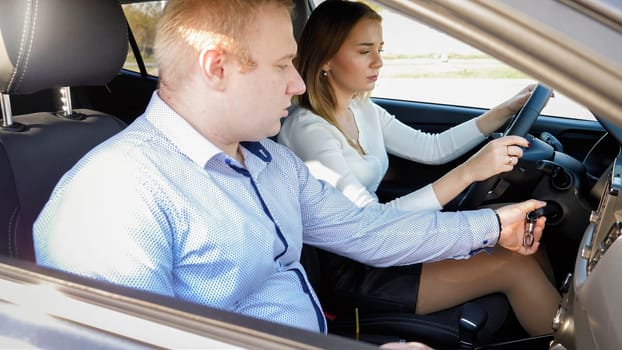 Portrait of male driving instructor teaching young woman how to power the car engine with key.