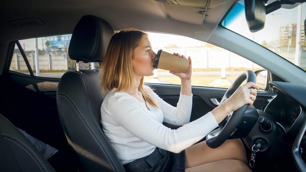 Beautiful blonde woman drinking coffee in car while commuting to work.