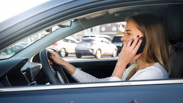 Portrait of irresponsible female driver talking by phone while driving a car in city.