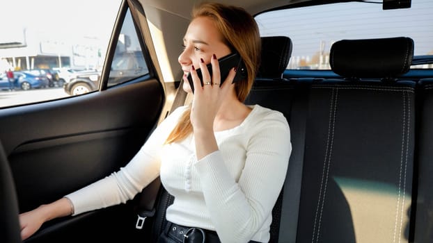 Beautiful businesswoman talking by smartphone and looking out of the car window while riding to work at morning.