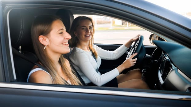 Portrait of female driver talking to smiling woman sitting on passenger seat while driving a car.
