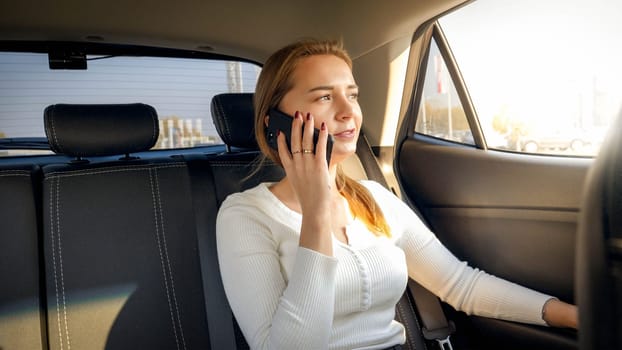 Portrait of beautiful blonde businesswoman talking by phone while riding on car back seat.