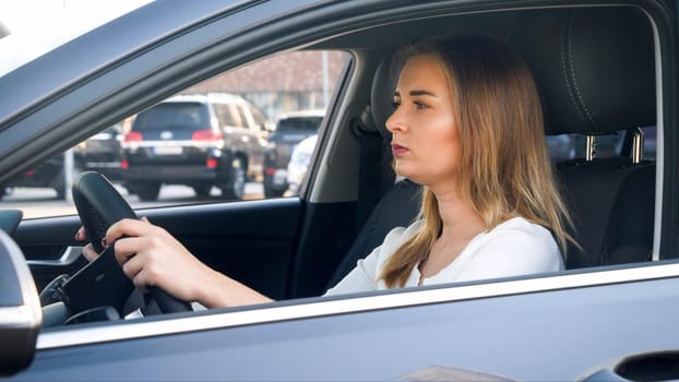 Portrait through open car window of young concentrated woman driving a car.