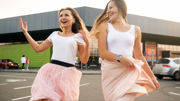 Portrait of two laughing cheerful girls in same outfit playing and having fun on car parking at shopping mall.