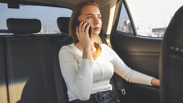 Toned portrait of young businesswoman having phone talk on taxi car back seat.