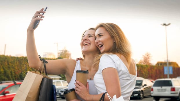 Portrait of two happy smiling girls making on smartphone with paper shopping bags.