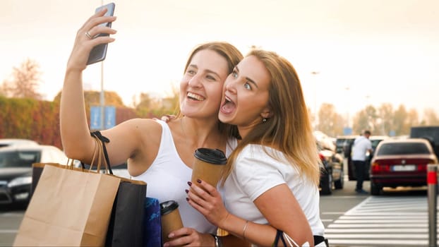 Portrait of two girls smiling and making faces while making selfie on smartphone after shopping in mall.