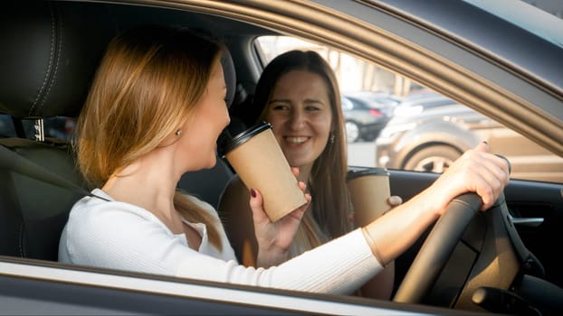 Portrait of two girl friends drinking coffee in car.