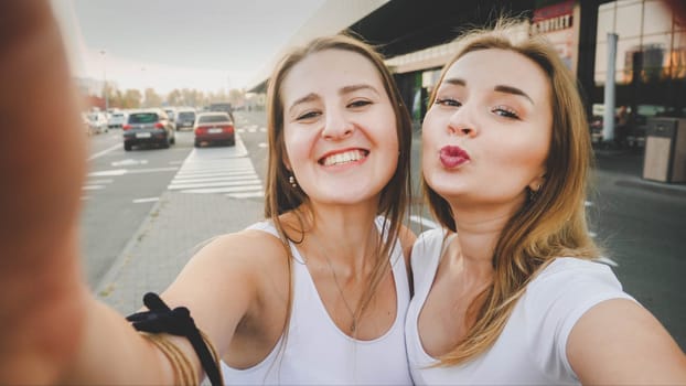 Toned selfie photo for social media of two smiling girls on car parking at shoping mall.