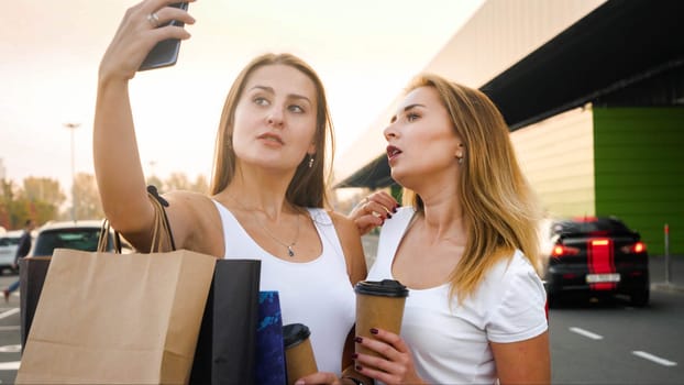 Portrait of two stylish sexy girls making selfie photo on smartphone at shopping mall entrance.
