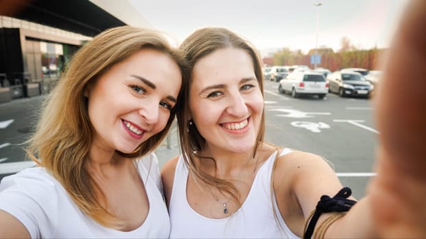 Closeup portrait of two smiling girls on car parking at shopping mall.