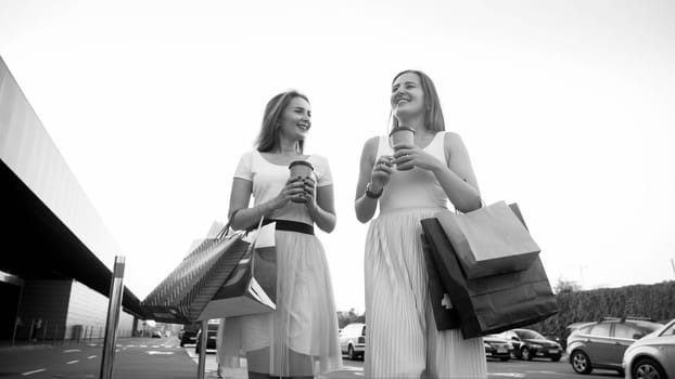 Black and white portrait of two girls with shoppings bags on car parking after doing shopping in mall.