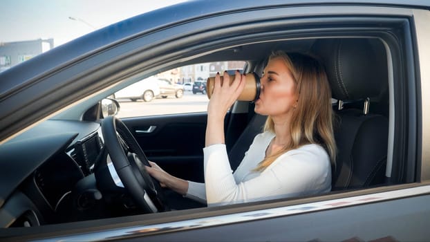 Portrait of beautiful young woman drinking coffee-to-go while driving a car at morning.