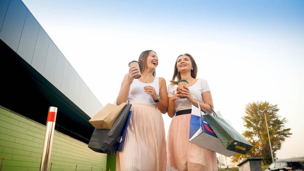 Two happy smiling girls with paper bags walking on street after doing shopping in mall.