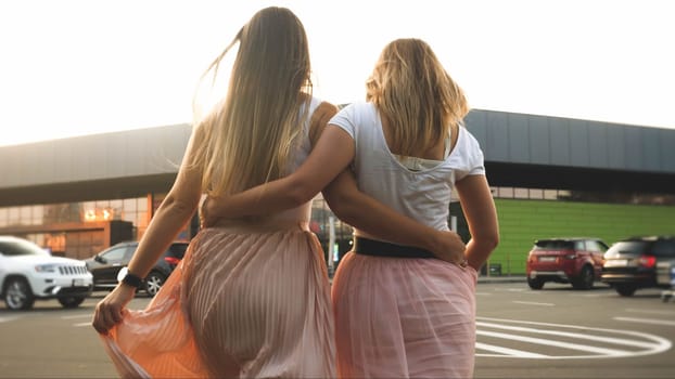Toned photo of two girls friends hugging while walking on car parking at shopping mall.