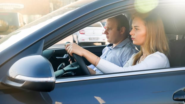 Portrait of young concentrated woman driving a car with her young husband sitting on passenger seat.