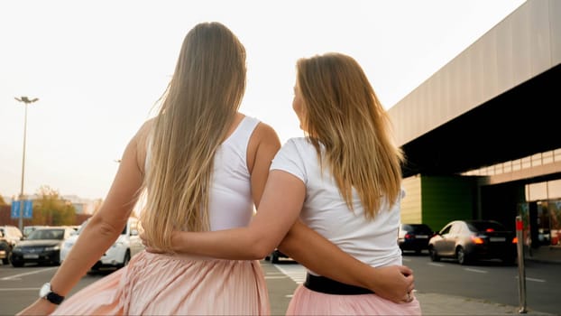 Rear view photo of two blonde girls embracing and olding each other at sunset.