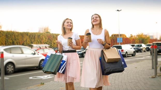 Portrait of female friends with shopping bags walking on car parking at big shopping mall.