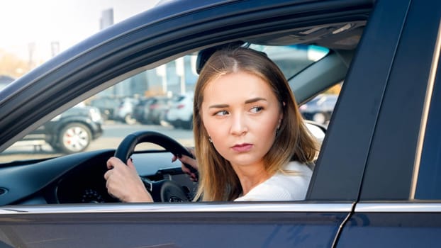 Portrait of young blonde woman looking for the parking place while driving a car.