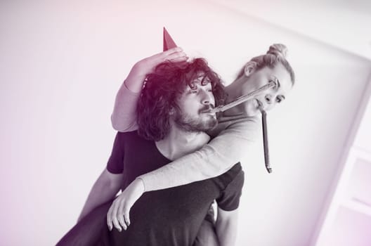 Young happy couple in party hats blowing in whistle isolated on a white background