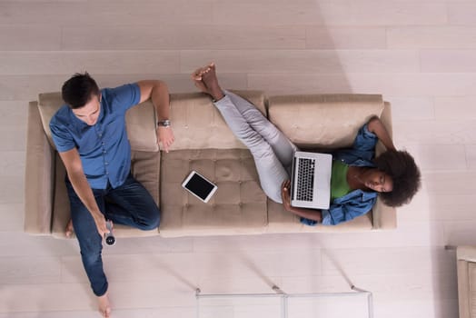Young multiethnic couple relaxes on the sofa in the luxury living room, using a tablet and remote control top view